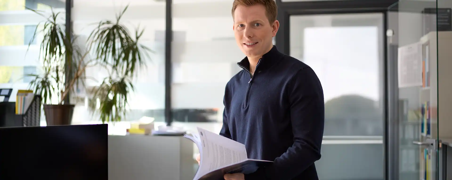 Ein Mann steht in einem Büro und hält Unterlagen in den Händen