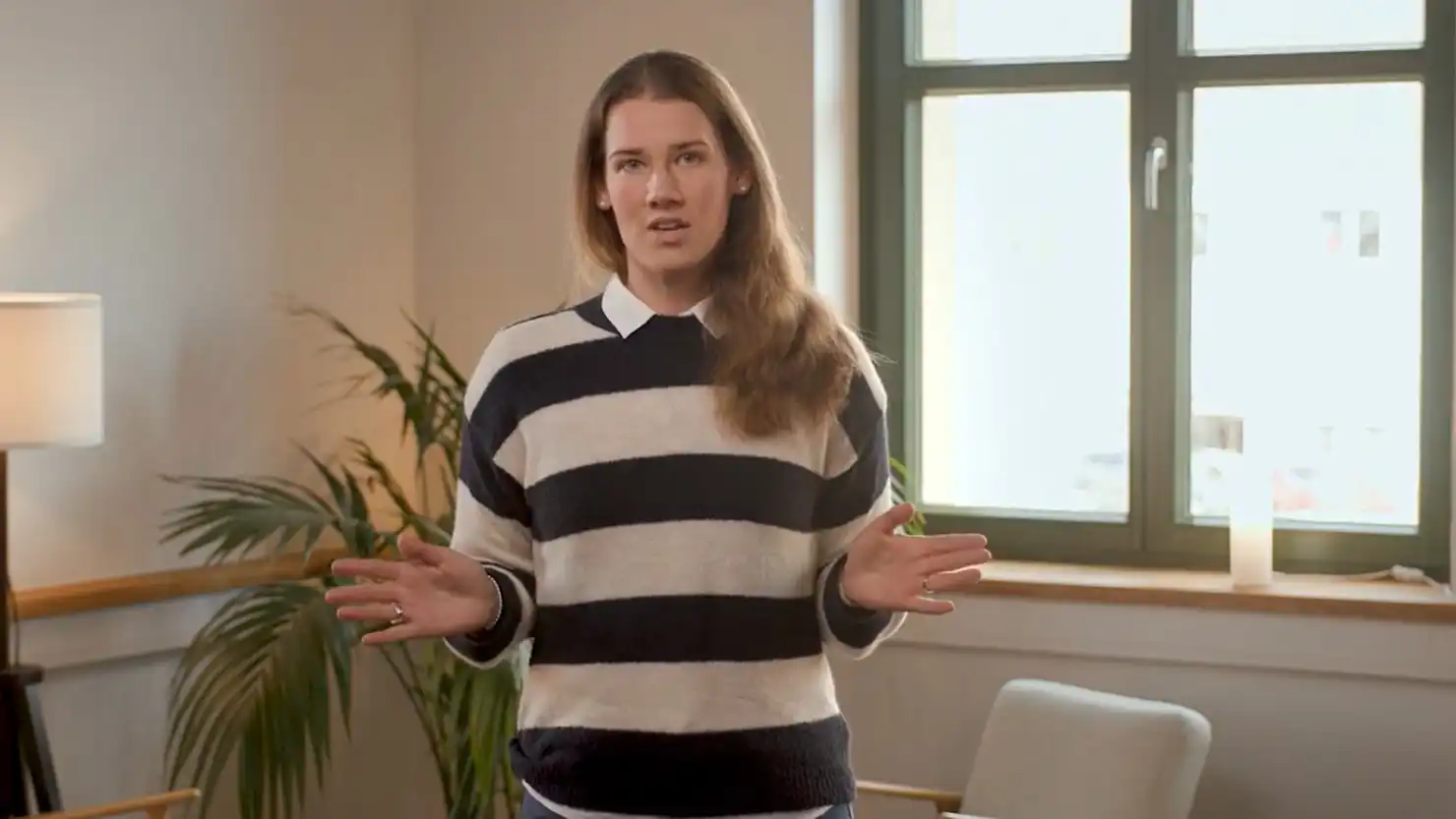 Eine Frau im gestreiften Pulli steht vor einer Sitzecke